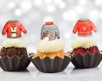 May include: Three cupcakes decorated with festive Christmas sweater toppers. The cupcakes are topped with white frosting and are in black cupcake liners. The sweaters are red and gray with different designs, including a reindeer, a bear, and a heart.