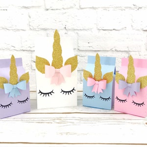 Unicorn milk carton party boxes. The unicorn party boxes display a unicorn face with eyelashes, a cute bow near the horn and the ears and horn in glitter gold. The party boxes come in pink, powder blue, white and lavender, in different sizes.