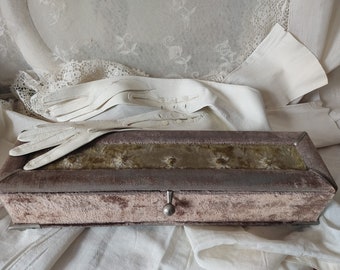 Puede incluir: Un joyero de terciopelo vintage con tapa con bisagras y cierre de metal. La caja está forrada con tela de terciopelo verde y tiene un interior de satén blanco. La caja está sobre un mantel de encaje blanco.