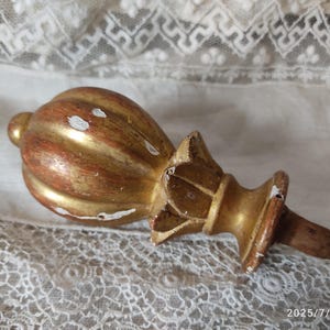 May include: An antique finial in gold and reddish-brown tones. The bulbous top has vertical ridges, and the base is star-shaped. The wooden piece shows signs of wear, with some white paint chipping. A decorative element.