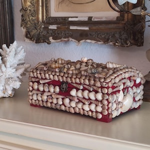 May include: A rectangular box decorated with a variety of seashells, featuring a red interior and a small metal clasp. The box is covered in different types of shells, creating a textured surface. A decorative item.