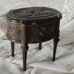 May include: A small, oval-shaped wooden jewelry box with intricate carvings. The box has three legs and a hinged lid with a floral design.