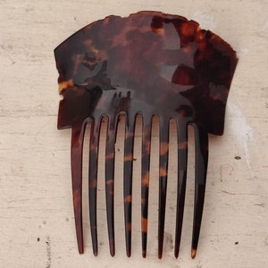 Könnte beinhalten: Ein brauner Schildpattkamm mit einem dekorativen Oberteil und sieben Zähnen.