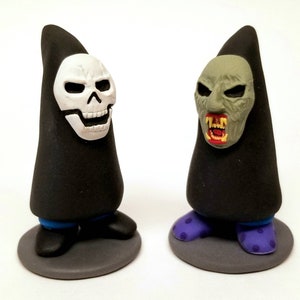 May include: Two black and gray Halloween gnome figurines with different masks. One gnome has a white skull mask and the other has a green monster mask.