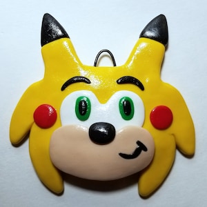 May include: Yellow and black clay ornament of a cartoon character with green eyes, a black nose, and red cheeks.