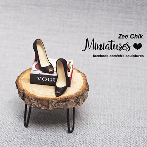 May include: Black high heel shoes with peep toes sitting on a wooden stand with a miniature Vogue magazine. The stand is on a gray textured surface. Zee Chik Miniatures is written in black cursive with a black heart.