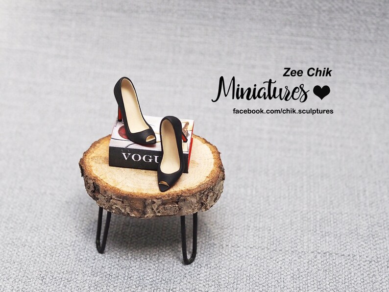 May include: Black high heel shoes with peep toes sitting on a wooden stand with a miniature Vogue magazine. The stand is on a gray textured surface. Zee Chik Miniatures is written in black cursive with a black heart.