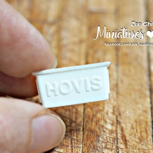 May include: White miniature sign with the word "HOVIS" embossed on it. The sign is held in a hand.