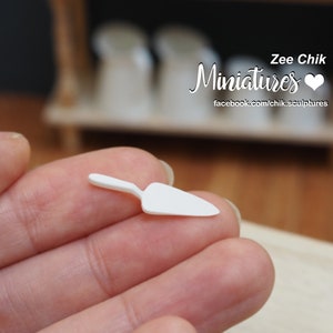 Può includere: Una piccola spatola di plastica bianca, uno strumento utilizzato per stendere e lisciare materiali come malta o gesso, tenuta in una mano.
