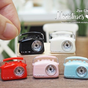May include: Five miniature vintage-style radios in different colours: black, white, red, pink, and blue. Each radio has a silver handle, a silver dial, and the word "RADIO" printed on the front.