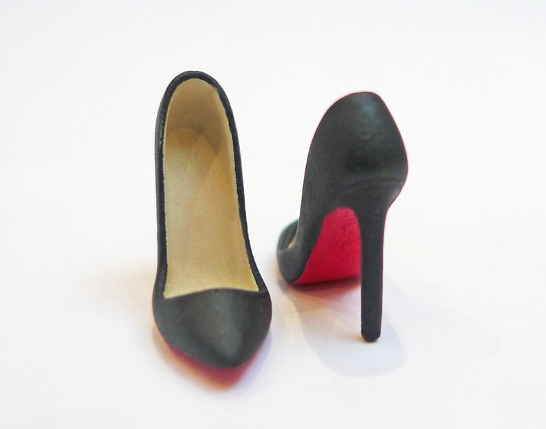 May include: A pair of black high-heeled shoes with red soles. The shoes are made of a smooth material and have a pointed toe.