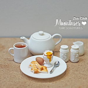 May include: A miniature tea set with a white teapot, teacup and saucer, a salt and pepper shaker, and a plate with a miniature egg and toast. The set is on a brown surface. Zee Chik Miniatures CHIK SCULPTURES