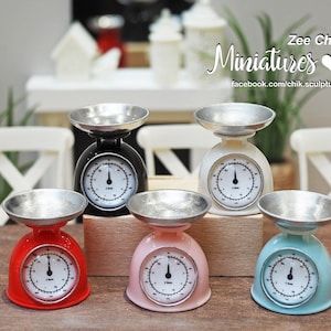 May include: Miniature kitchen scales in black, white, red, pink, and blue. Each scale has a silver-colored bowl and a circular gauge with a needle. The scales are decorative and feature the text "Zee Chik Miniatures" on the image.