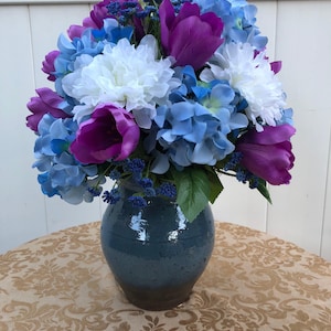 May include: A blue ceramic vase filled with a bouquet of purple tulips, white chrysanthemums, and blue hydrangeas.