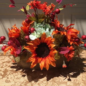May include: A fall-themed centerpiece with sunflowers, red berries, and green hydrangeas in a wooden bowl.