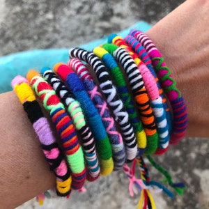 Può includere: Un set di braccialetti intrecciati colorati con diversi motivi e design. I braccialetti sono realizzati in filo e presentano una varietà di colori, tra cui rosa, blu, verde, giallo, rosso e nero.