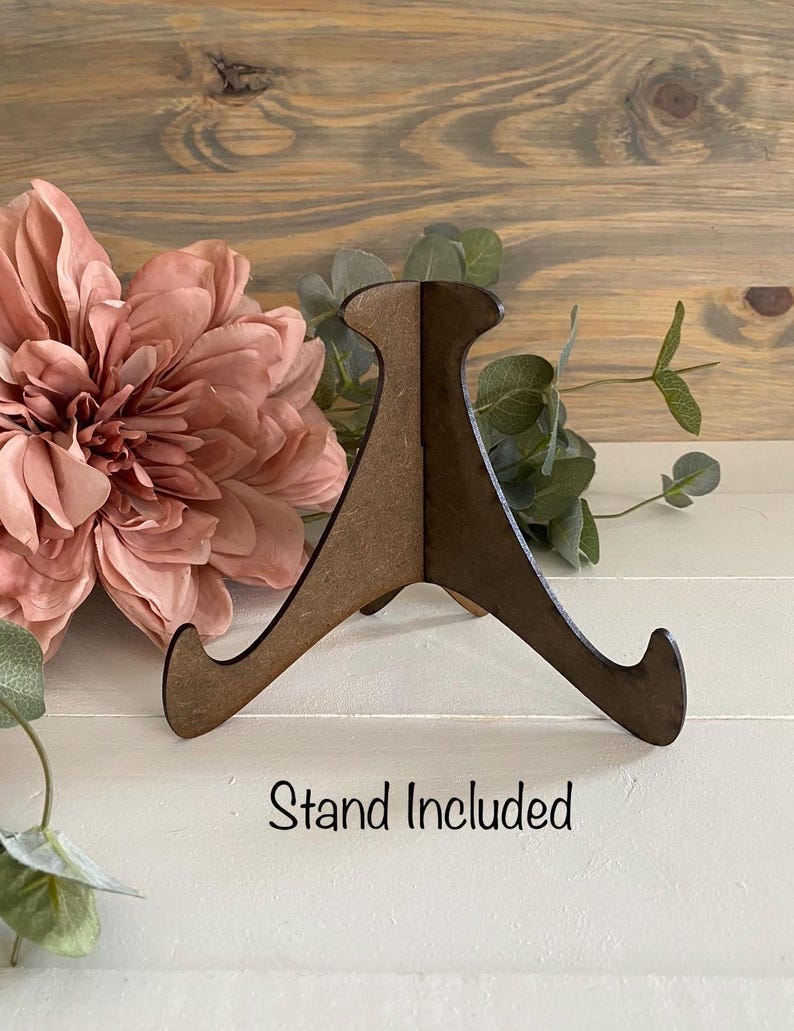 May include: A wooden stand with three legs, designed to hold a plate or other flat object. The stand is brown and has a simple design. The text "Stand Included" is printed below the stand.
