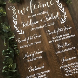 Puede incluir: Un letrero de madera con letras blancas anunciando una boda para Katelynn y Michael el 1 de diciembre de 2018. El letrero enumera los nombres de los padres de la novia y el novio, la dama de honor, las damas de honor, el padrino de boda y los padrinos de boda.