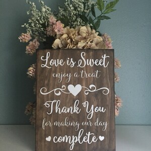 May include: A rustic wooden sign with the text "Love is Sweet enjoy a treat" and a heart symbol. Below the text is "Thank You for making our day complete" with two heart symbols.