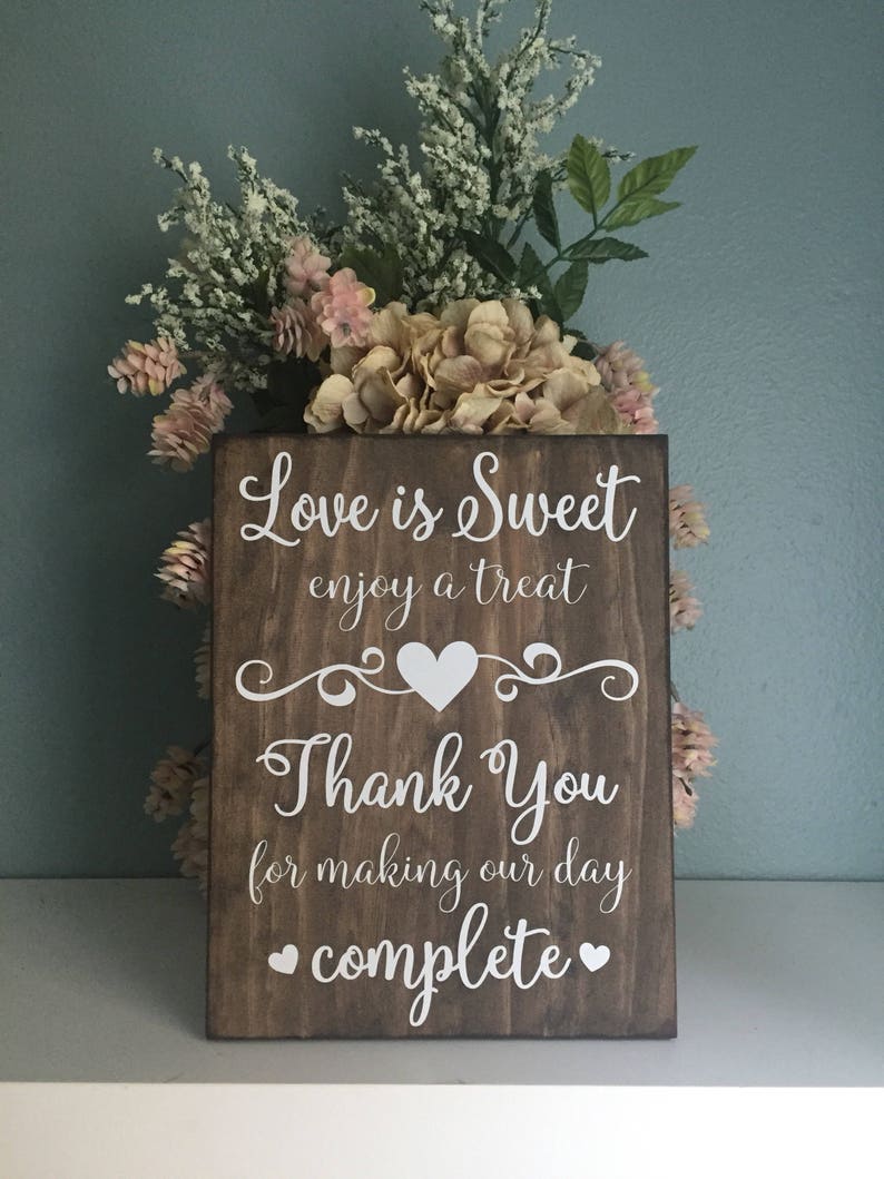 May include: A rustic wooden sign with the text "Love is Sweet enjoy a treat" and a heart symbol. Below the text is "Thank You for making our day complete" with two heart symbols.