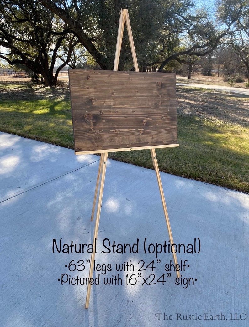 May include: A natural wood easel stand with a brown wooden sign. The stand has 63-inch legs and a 24-inch shelf. The sign is 16 inches by 24 inches.