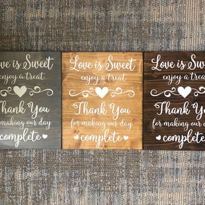 May include: Three wooden signs with the text "Love is Sweet enjoy a treat Thank You for making our day complete" in white lettering on a dark gray, light brown, and dark brown background.