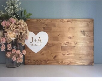 May include: A wooden sign with a white heart cutout. The heart has the text "J+A 08.27.17" in gold lettering.