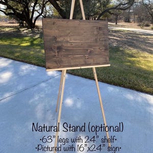 May include: A wooden easel with a dark brown sign. The easel has natural wood legs and a 24-inch shelf. The sign is 16x24 inches. The text on the image says "Natural Stand (optional)" and "63" legs".