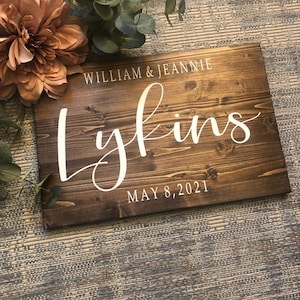 May include: A rustic wooden sign with the text "William & Jeannie Lykins May 8, 2021" in white lettering.