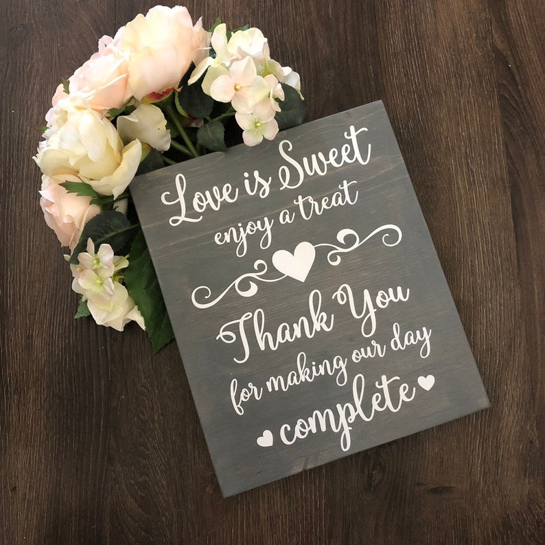 May include: Gray wooden sign with white text that reads "Love is Sweet enjoy a treat Thank You for making our day complete" with a heart symbol between each line of text.