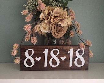 May include: A wooden sign with the date 8-18-18 written in white paint with a heart between each number. The sign is brown and has a rustic look.