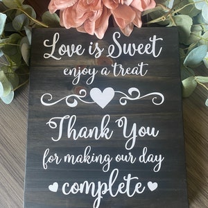 May include: A dark wood sign with white text that reads "Love is Sweet enjoy a treat Thank You for making our day complete" with a heart shape between the words "Thank You".