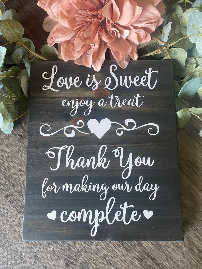 May include: A dark wood sign with white text that reads "Love is Sweet enjoy a treat Thank You for making our day complete" with a heart shape between the words "Thank You".