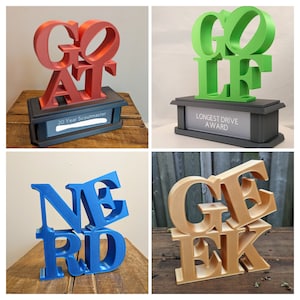 May include: Four different 3D printed trophies, each with a different word spelled out in a unique way. The words are "GOAT", "GOLF", "NERD", and "GEEK". The trophies are made of different colors, including red, green, blue, and gold.
