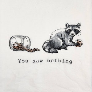 K&ouml;nnte beinhalten: Eine Schwarzwei&szlig;illustration eines Waschb&auml;ren, der ein Keks h&auml;lt. Eine Dose mit Keksen liegt auf dem Boden, einige Kekse sind herausgefallen. Der Text "You saw nothing" befindet sich unter dem Waschb&auml;ren.