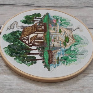 May include: Embroidered hoop art featuring a cottage with a brown roof and white walls surrounded by green trees. The cottage has a chimney with smoke coming out of it. The background is a light blue sky with white clouds.