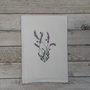 Könnte beinhalten: Ein weißes Küchentuch mit einem gestickten Design aus Lavendelblüten und Bienen.