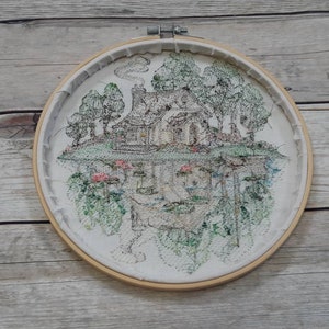 May include: Embroidered hoop art featuring a black and white illustration of a house with trees and flowers. The house is upside down and the trees and flowers are right side up.