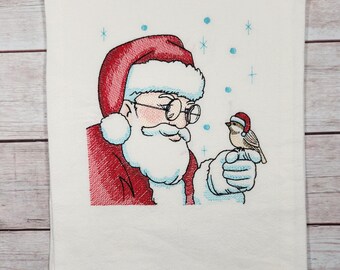 Op de afbeelding: Geborduurde keukendoek met Sinterklaas met een witte baard en een rode muts, die naar een klein bruin vogeltje met een rode muts kijkt. De achtergrond is wit met blauwe sneeuwvlokken.