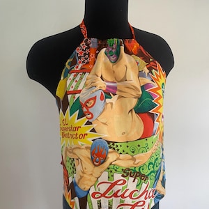 May include: A halter top with a vibrant print of Luchadores, or Mexican wrestlers. The design showcases masked wrestlers in action poses, with text reading "El Superstar Destructor" and "Super Lucha Libre". The top is displayed on a black mannequin.