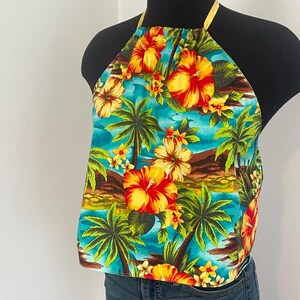 May include: A halter top with a tropical floral print featuring red, yellow, and orange hibiscus flowers, palm trees, and a blue ocean scene. The top has a yellow neck strap and is made of a lightweight fabric.
