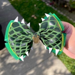 May include: Green and white bow with a crocodile pattern and a small gold clock charm.