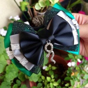 May include: A black and green bow with silver glitter and a silver snake charm. The bow is made of satin and tulle.