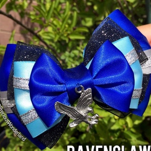 May include: A blue and silver bow with a silver raven charm. The bow is made of satin ribbon and has a black mesh overlay. The charm is attached to the center of the bow with a silver loop. The bow is perfect for adding a touch of Harry Potter fandom to your outfit.