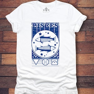 May include: White t-shirt with a blue graphic of the Pisces zodiac sign. The graphic includes two fish, stars, and the text "Pisces" with the dates "Feb 19" and "Mar 20".