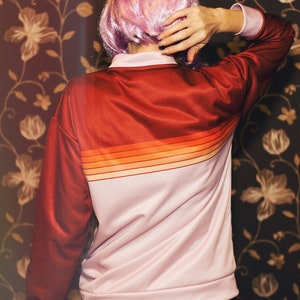 May include: A pink and red striped jacket with long sleeves and a zipper closure. The jacket is made of a soft, smooth fabric.