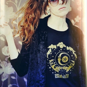 May include: A woman wearing a black velvet jacket over a black t-shirt with a gold moon and stars design. The t-shirt also has the text "LILA LANG" in gold lettering.