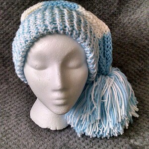 May include: A blue and white knitted hat with a long, fluffy tassel. The hat is made with a striped pattern and has a simple, classic design.