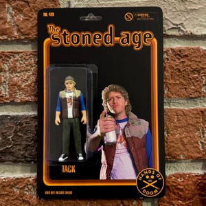 May include: Action figure packaging for "The Stoned-Age" featuring a figure named "Tack" in a blue and brown outfit. The packaging includes the text "Hands of Doom" and "Does Not Include Chicks."