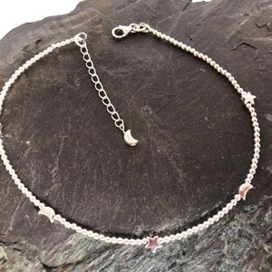 May include: A silver chain necklace with a delicate beaded design and small star and crescent moon charms.